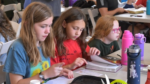 three little girls seated at a table with an open Bible and notebook