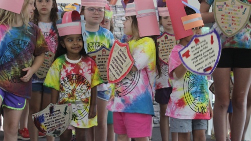 children in tie-dye shirts wearing paper helmets and pretend shields