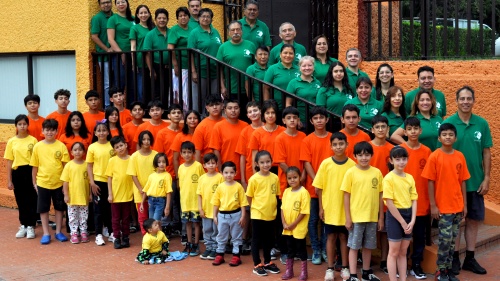 a large group of people standing outside, some lined up on a staircase, some in front of it, all wearing one of three colors of matching shirts