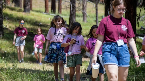 a line of girls walking through the grass and wearing matching pink shirts