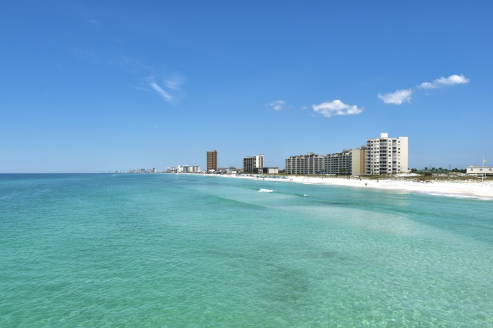 a clear ocean with the shoreline and city buildings in the background