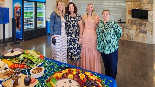 four ladies gathered by a table of colorful food