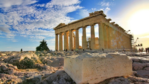 Ancient ruins of the Parthenon with tourists by the structure and a large block of stone in the foreground