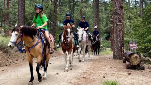 a group of girls riding horses in the woods