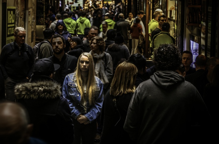 A woman walking in a crowded alley with numerous people.