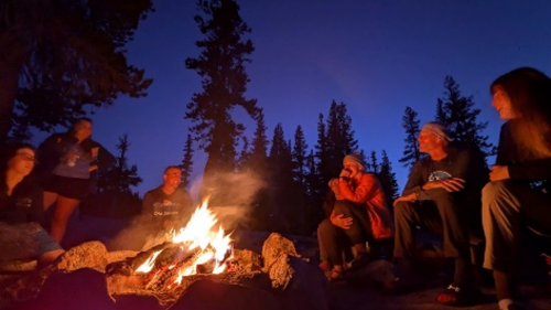 a group of people sitting outside in the dark around a glowing campfire